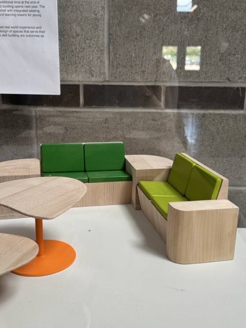 This is an image of a mini furniture set by Sheridan Furniture students. The materials observed here appears to be wooden for the base of the chairs and top of the table with a plastic material as the accent, in green, lime green, and orange.