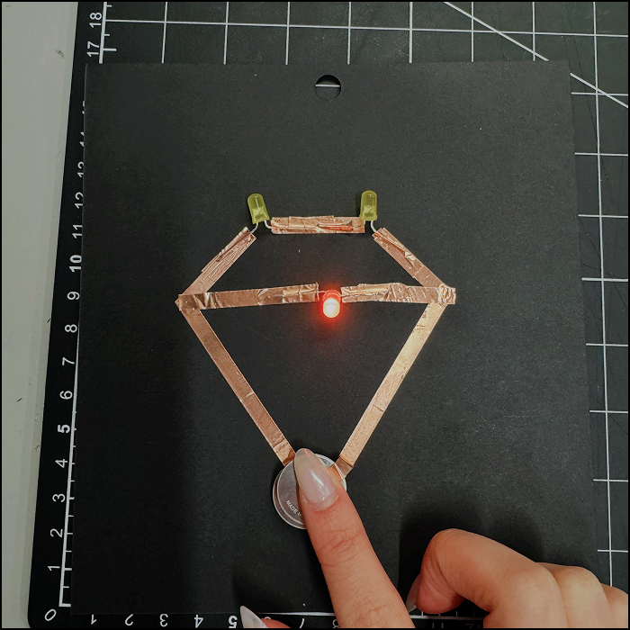 Image of experimentation, modified series circuit with another light addedd in a parallel circuit style with positive side of the copper tape not fully pressed on the battery.